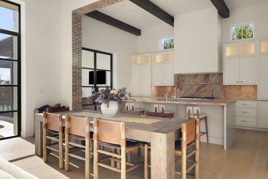 Kitchen featuring glass fronted cabinets, white cabinetry, backsplash, light stone countertops, and a kitchen island with sink