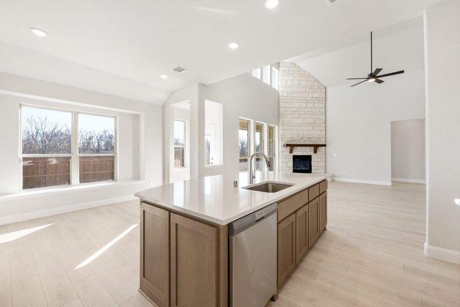 Kitchen island with sink and dishwasher, open to living area with stone fireplace and vaulted ceiling
