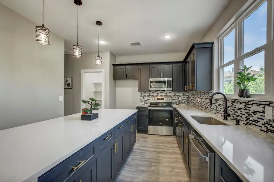 Kitchen with stainless steel appliances, pendant lighting, tasteful backsplash, light wood-style flooring, and light stone countertops