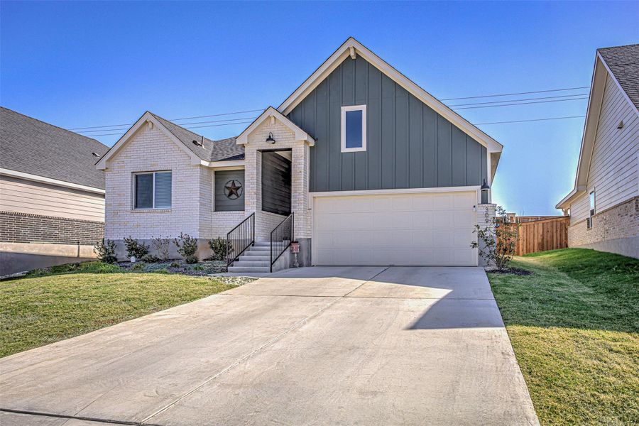View of front of house with board and batten siding, driveway, a garage, and brick siding