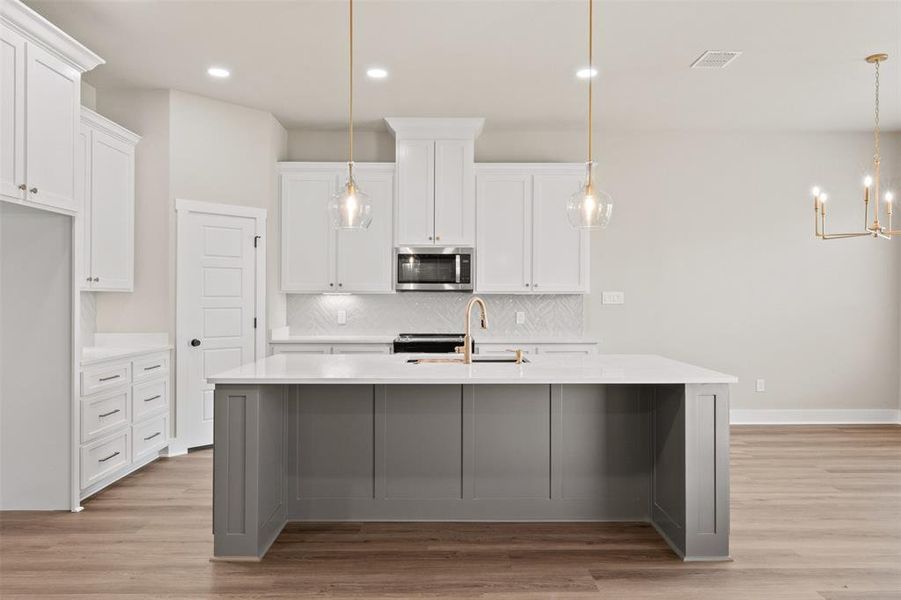 Dual tone kitchen with light wood finished floors, a center island with sink, light stone countertops, stainless steel microwave, and dual tone cabinets