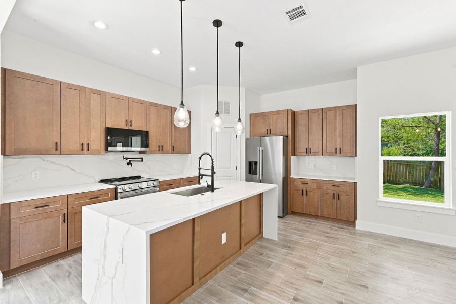 Expansive waterfall quartz kitchen island with an undermount sink and a sleek matte black gooseneck faucet.