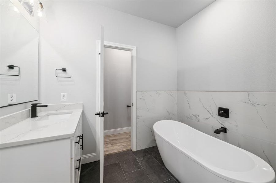 Bathroom featuring vanity, a soaking tub, tile walls, and a wainscoted wall Bathroom featuring vanity, a soaking tub, tile walls, and a wainscoted wall