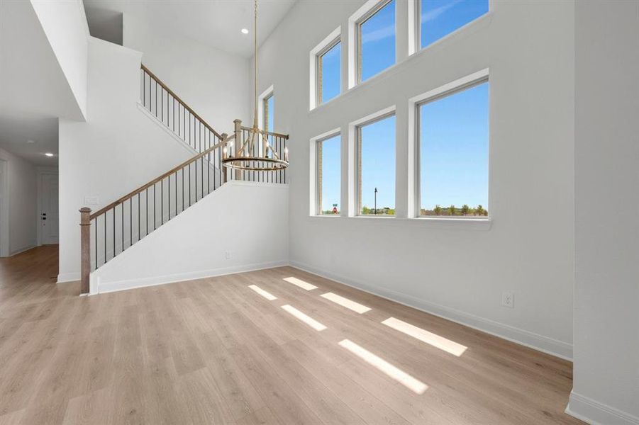 Double-height room featuring wood-finish flooring, a contemporary chandelier, a staircase with wood-toned handrails and black balusters, and multiple large windows