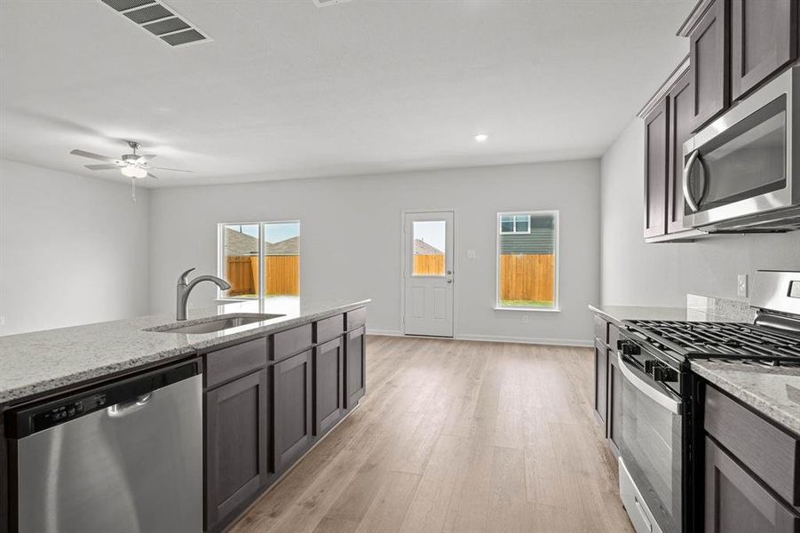 Kitchen with appliances with stainless steel finishes, light stone counters, light wood finished floors, a ceiling fan, and recessed lighting