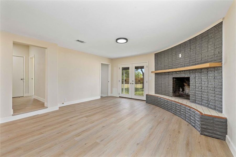 Unfurnished living room featuring french doors, a brick fireplace, and light wood-style flooring Unfurnished living room featuring french doors, a brick fireplace, and light wood-style flooring