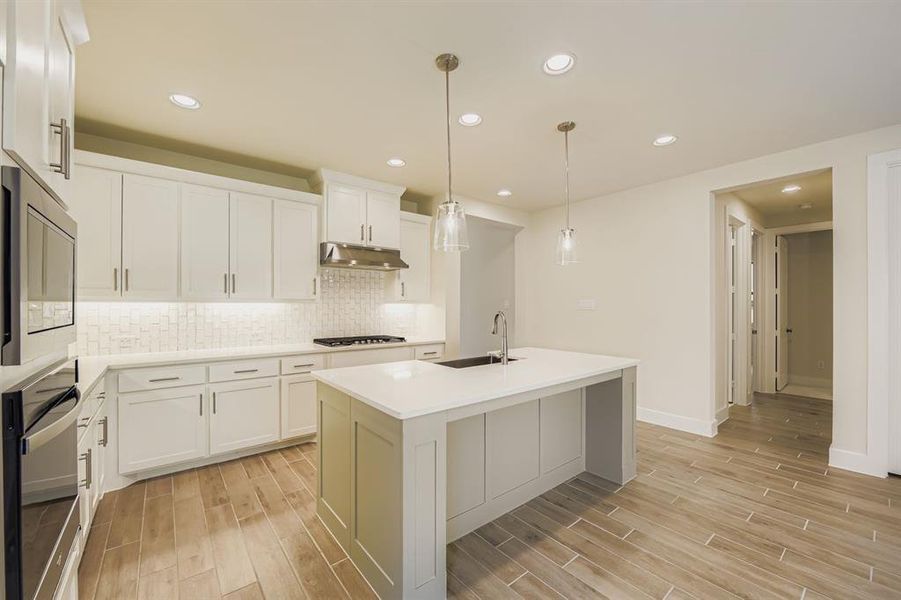 Kitchen featuring white cabinets, decorative backsplash, recessed lighting, wood tiled floors, and hanging light fixtures