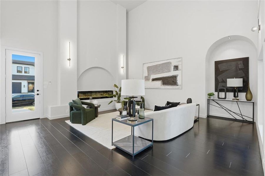 Spacious living area featuring high vaulted ceilings, dark wood-finish flooring, a modern horizontal fireplace, arched architectural details, and linear sconce lighting
