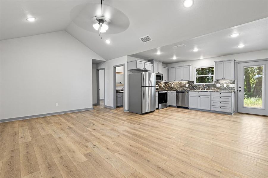 Kitchen featuring decorative backsplash, stainless steel appliances, gray cabinetry, open floor plan, and light wood finished floors Kitchen featuring decorative backsplash, stainless steel appliances, gray cabinetry, open floor plan, and light wood finished floors