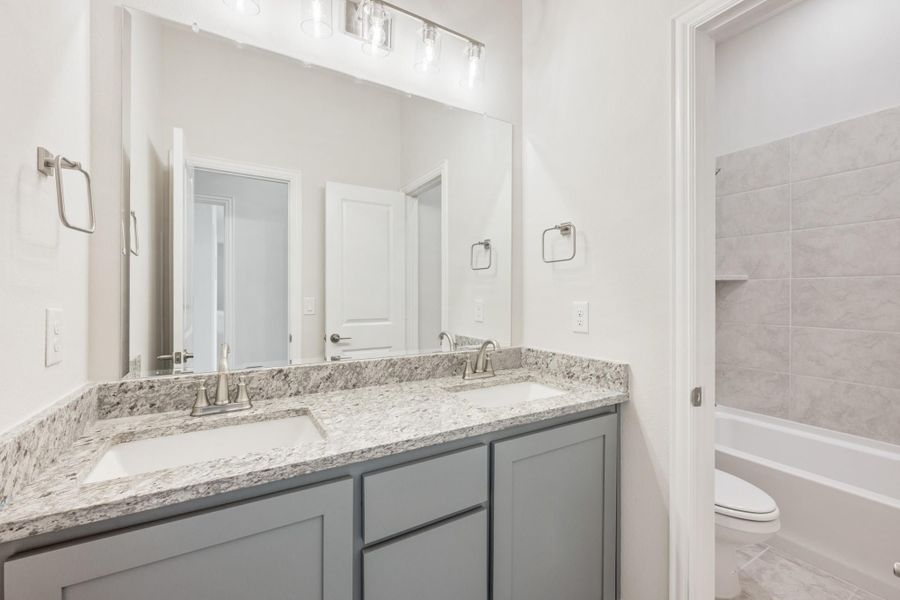 Bathroom with double sink vanity, gray cabinets, granite countertop, large mirror, and tiled tub-shower combo