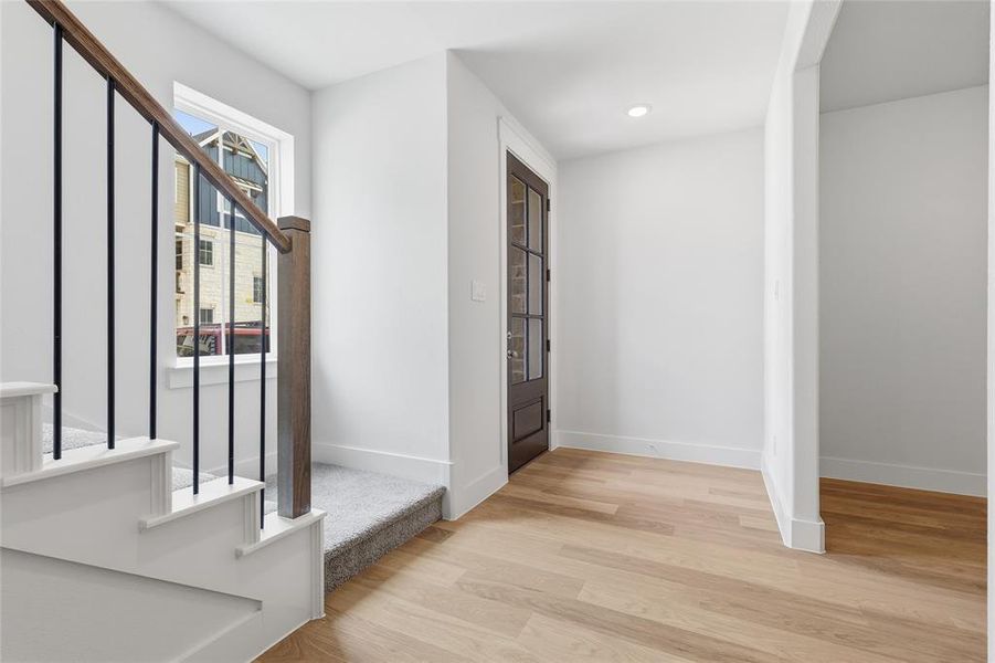 Entryway featuring light hardwood flooring and a staircase with white risers, carpeted treads, and a dark wood handrail with black balusters