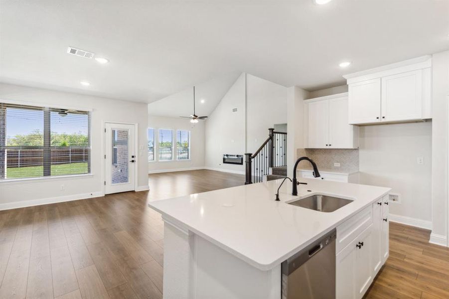 Kitchen featuring stainless steel dishwasher, white cabinetry, sink, and an island with sink