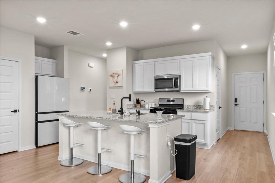 Kitchen with appliances with stainless steel finishes, light wood-type flooring, a kitchen breakfast bar, light stone counters, and white cabinetry