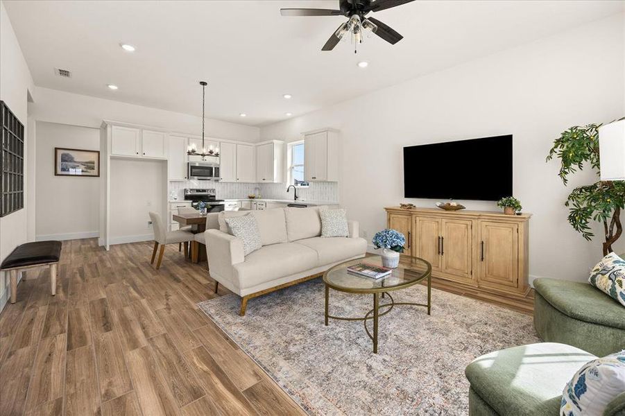 Open-concept living area featuring wood-finish flooring, white cabinetry, a kitchen with a tile backsplash, recessed lighting, and a ceiling fan