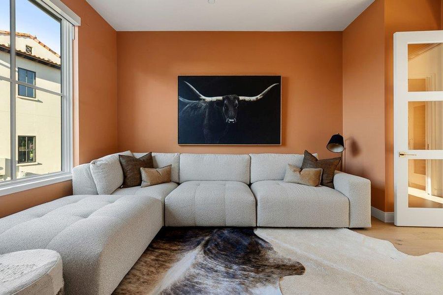 Inviting living space featuring warm-toned walls, a large window offering natural light, and light wood flooring