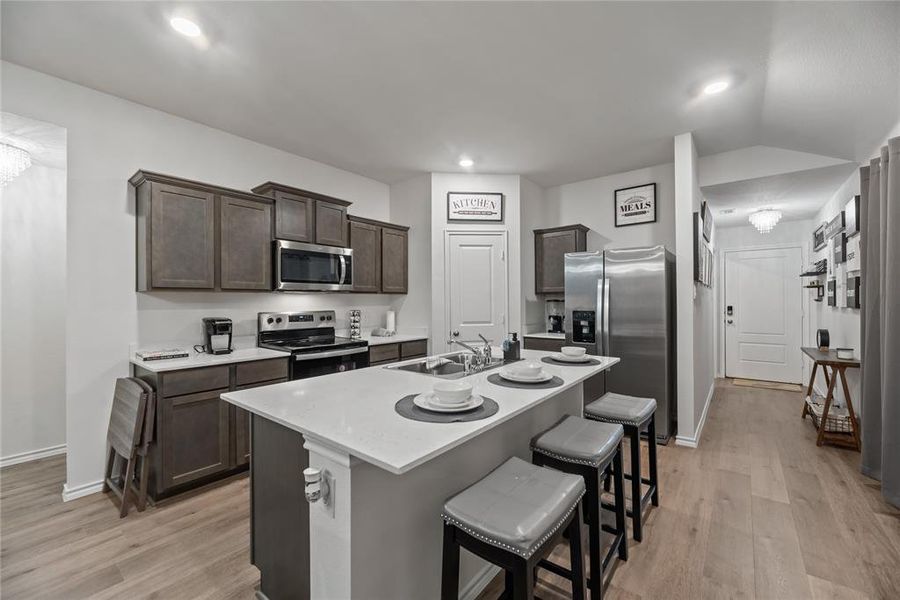 Kitchen featuring a kitchen bar, appliances with stainless steel finishes, dark brown cabinets, light wood finished floors, and recessed lighting