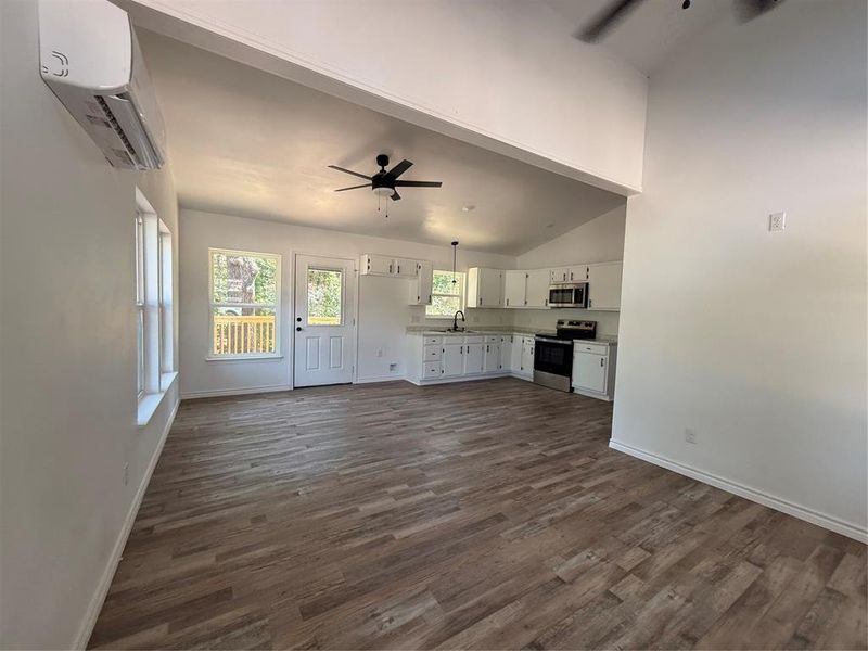 Unfurnished living room featuring ceiling fan, a wall mounted AC, dark wood-type flooring, and high vaulted ceiling