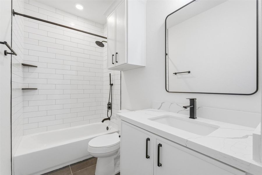 Guest bathroom with a shower-tub combo, neutral black and white finishes, & a cabinet above the toilet for added storage.