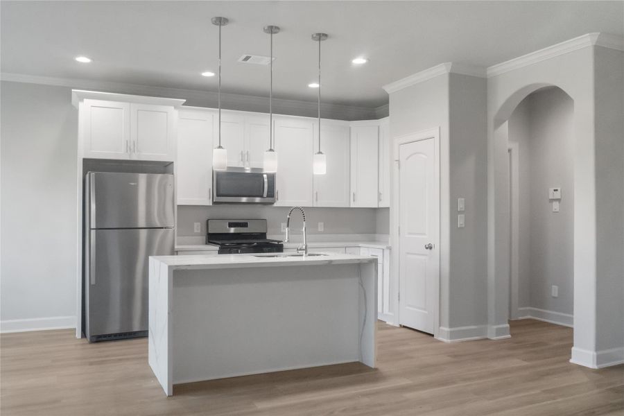 This photo showcases a modern kitchen with white cabinetry, stainless steel appliances, and a center island with pendant lighting. The space features light wood flooring and a neutral color palette, creating a bright and inviting atmosphere.