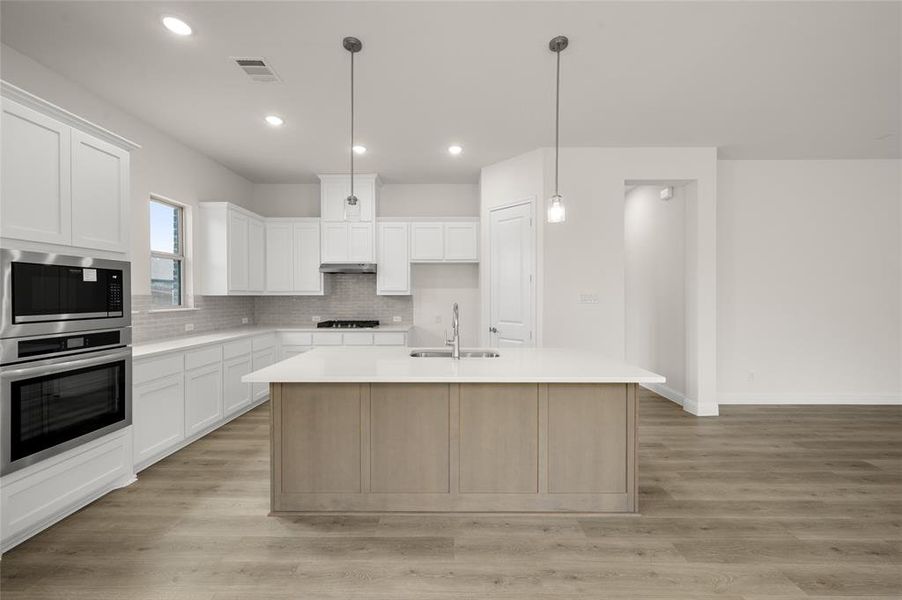 Kitchen featuring stainless steel oven, black microwave, gas cooktop, backsplash, and light countertops