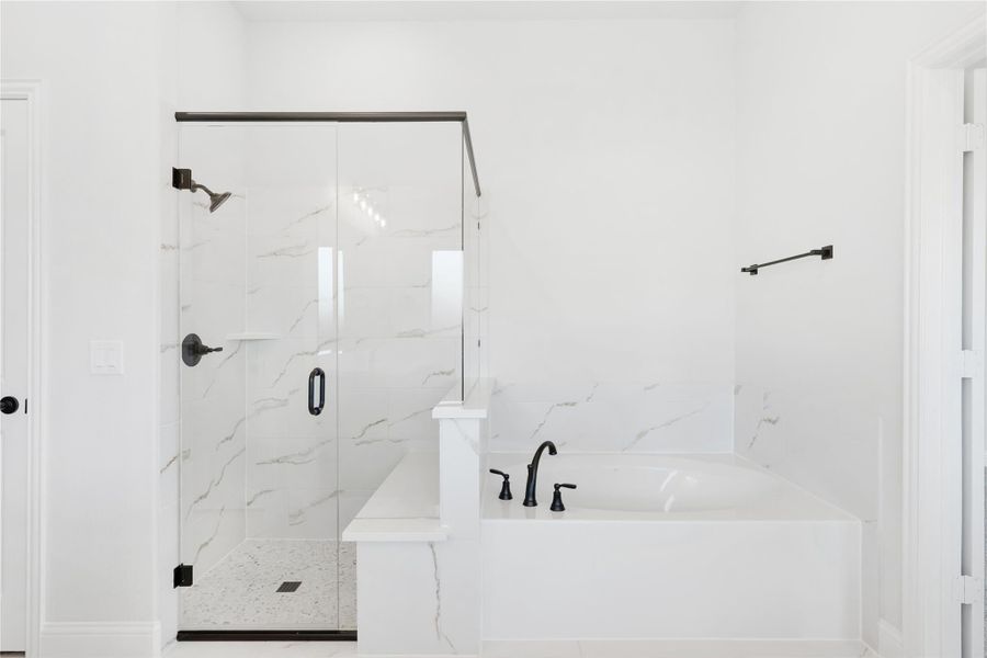 Bathroom with soaking tub and glass-enclosed shower featuring marble tile walls and matte black fixtures Bathroom with soaking tub and glass-enclosed shower featuring marble tile walls and matte black fixtures