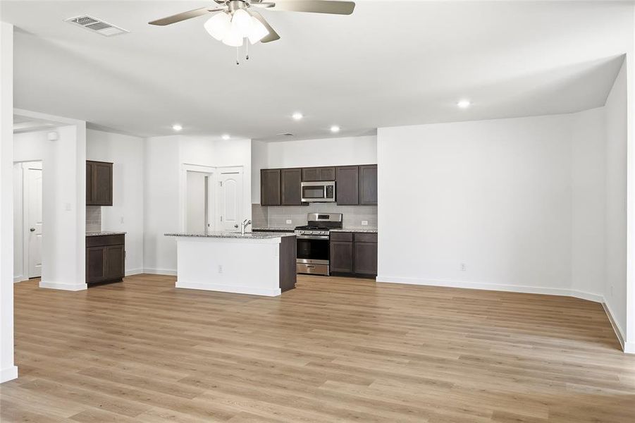Kitchen featuring a ceiling fan, stainless steel appliances, dark wood finish cabinets, a kitchen island with sink, and light wood-type flooring