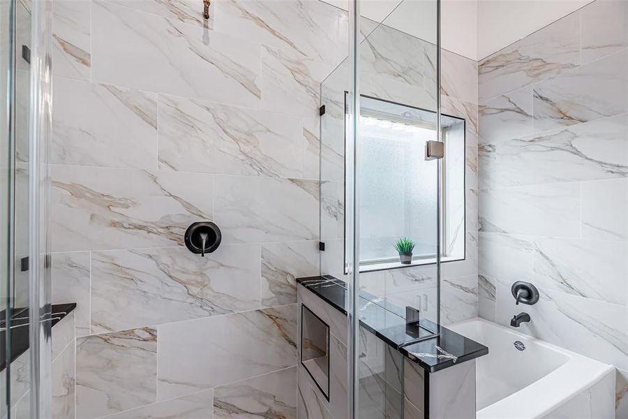 Primary modern bathroom featuring marble-style tiling, a glass-enclosed shower, and sleek black fixtures. A window allows for natural light.