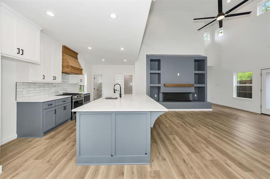 Kitchen with stainless steel range with gas cooktop, custom range hood, ceiling fan, open floor plan, and gray cabinets Kitchen with stainless steel range with gas cooktop, custom range hood, ceiling fan, open floor plan, and gray cabinets
