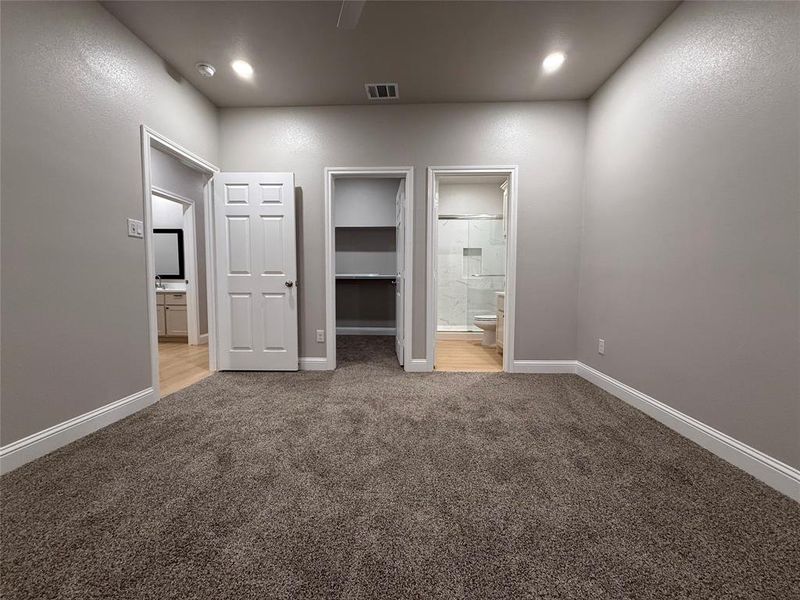 Unfurnished bedroom featuring a walk in closet, connected bathroom, light colored carpet, and a ceiling fan