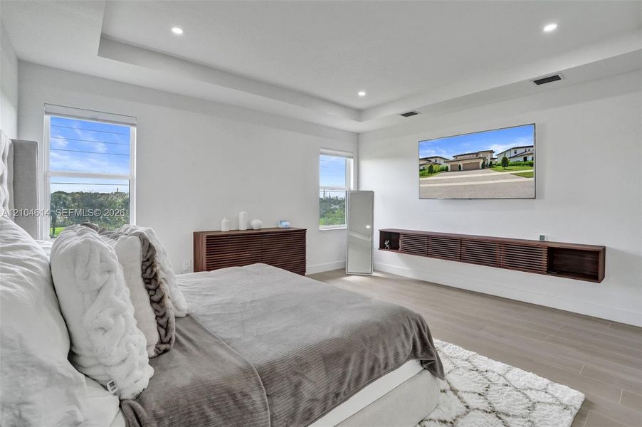Tray ceiling with recessed lighting, light wood-look flooring, and a built-in floating media cabinet