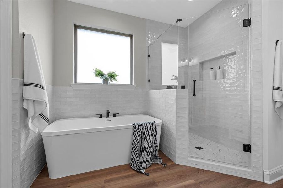 Full bath featuring tile walls, wood finished floors, a soaking tub, a stall shower, and wainscoting Full bath featuring tile walls, wood finished floors, a soaking tub, a stall shower, and wainscoting