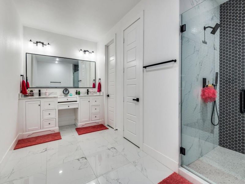 Bathroom featuring double vanity, a marble finish shower, and light marble finish floors