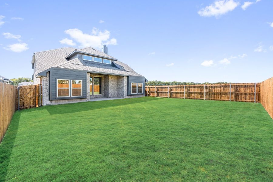 Backyard of a brick and gray siding home with large green lawn, patio, and wood privacy fence. Backyard of a brick and gray siding home with large green lawn, patio, and wood privacy fence.