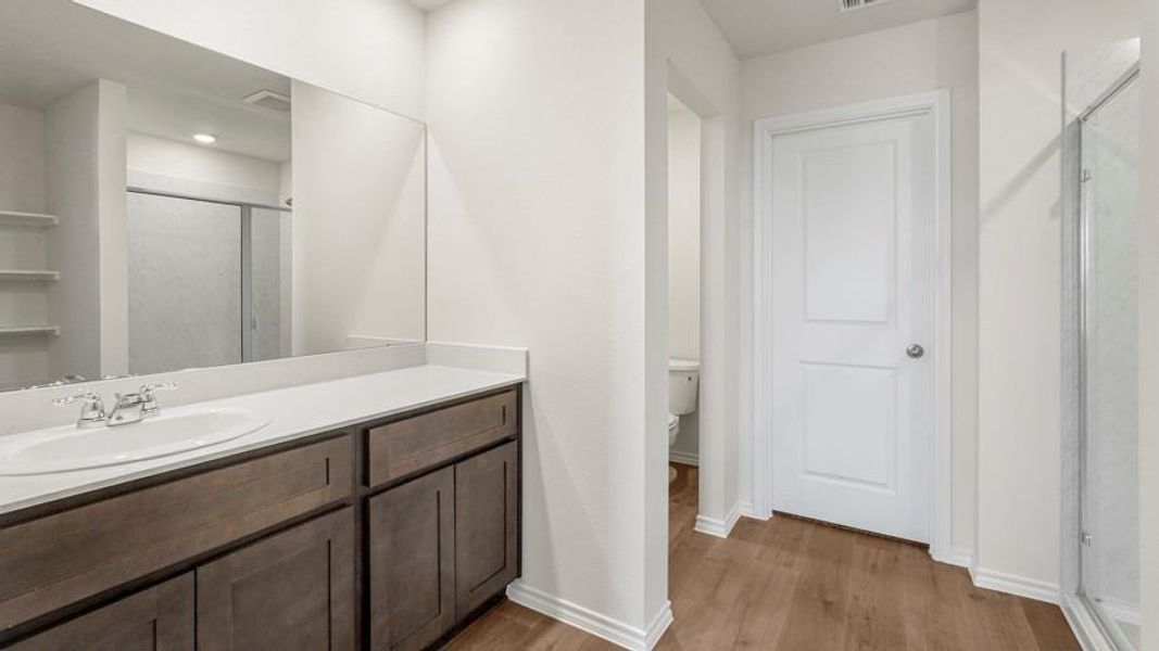 Bathroom featuring a single vanity with a white countertop and wood-finish cabinetry, a large wall-mounted mirror, and wood-finish flooring