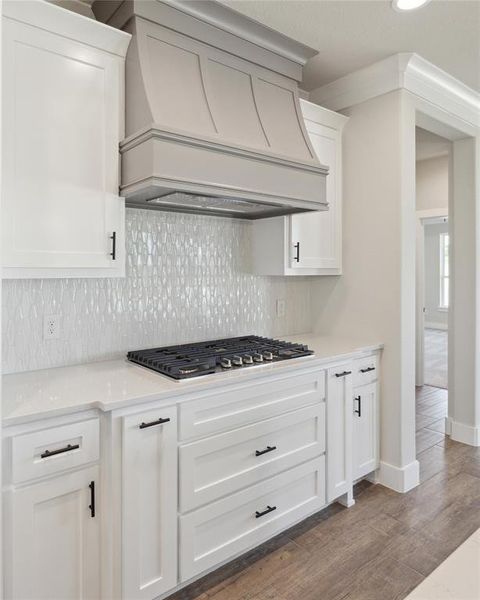 Kitchen with stainless steel gas stovetop, white cabinets, custom range hood, decorative backsplash, and dark hardwood / wood-style flooring