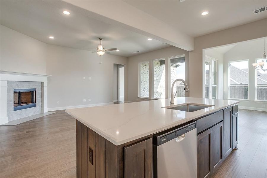 Kitchen featuring stainless steel dishwasher, sink, a kitchen island with sink, and light wood-type flooring