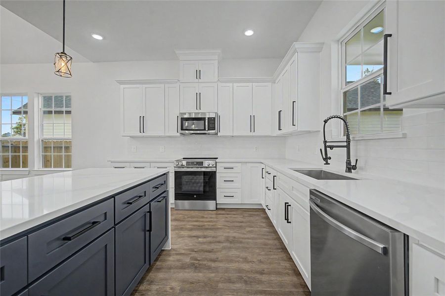 Bright modern kitchen with white cabinetry, stainless steel appliances, black hardware, and quartz-style counters.