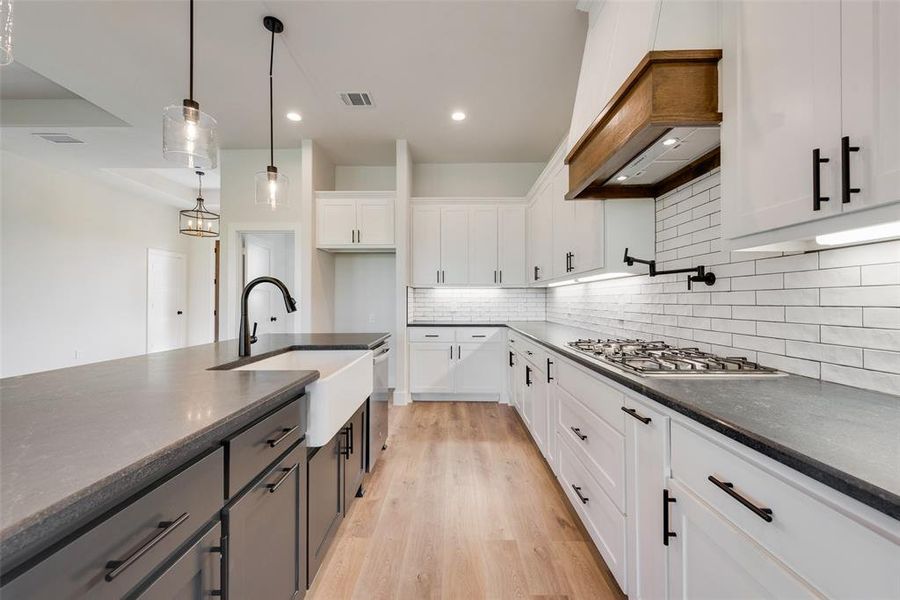 Kitchen with backsplash, white cabinets, hanging light fixtures, light wood-type flooring, and stainless steel appliances