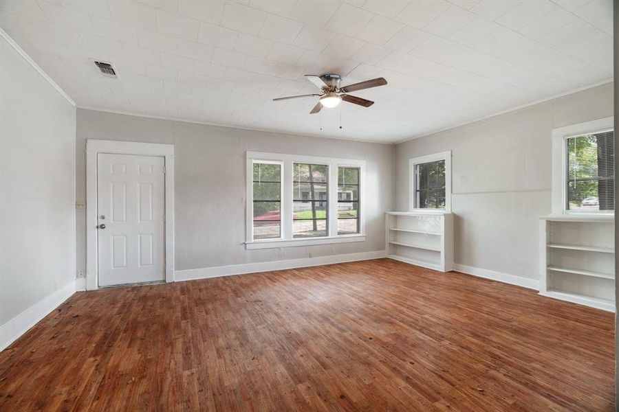 Unfurnished room featuring crown molding, hardwood / wood-style flooring, ceiling fan, and built in shelves Unfurnished room featuring crown molding, hardwood / wood-style flooring, ceiling fan, and built in shelves