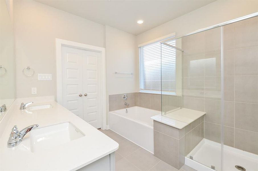 This bright and spacious bathroom features a double vanity, a large soaking tub, a separate glass-enclosed shower, and modern fixtures. The neutral tiles and ample natural light create a clean, inviting atmosphere.