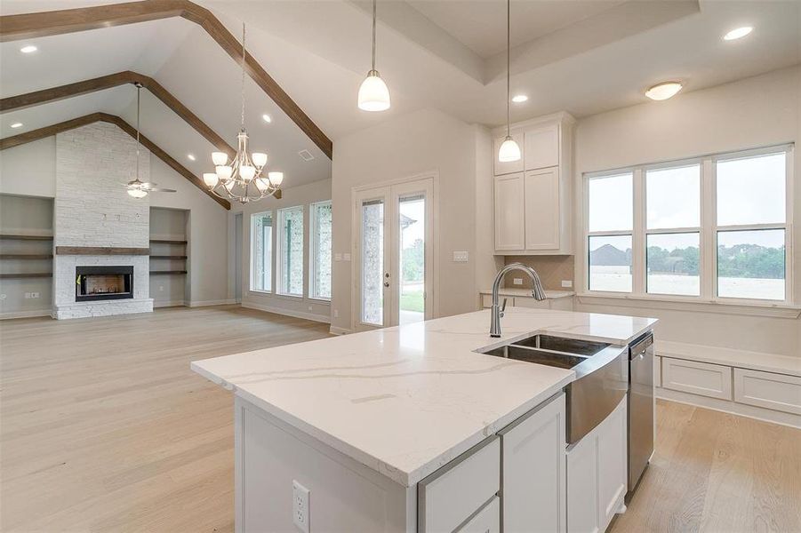 Kitchen with a stone fireplace, a kitchen island with sink, brick wall, and light hardwood / wood-style floors