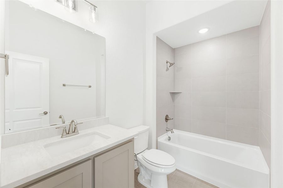 Bathroom with single vanity, quartz countertop, toilet, and tub-shower combo with gray tile surround