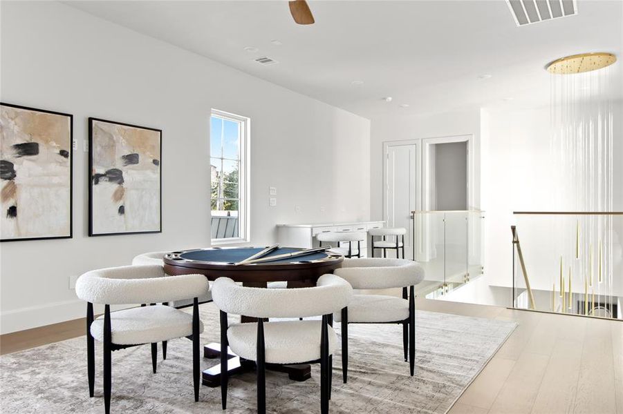 Spacious bonus room featuring light wood-finish flooring, a contemporary glass railing, a sleek built-in wet bar with seating, and a modern circular light fixture