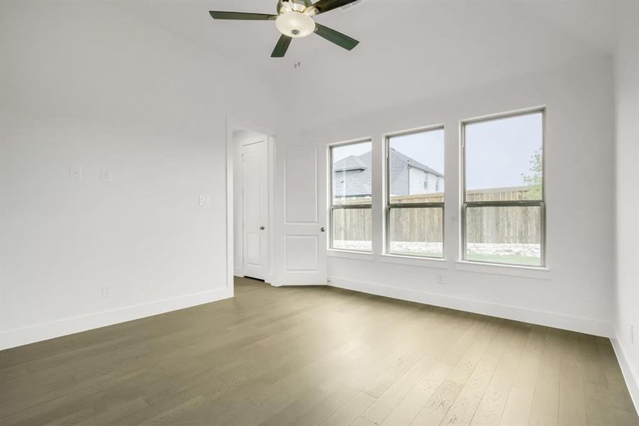 Spacious room featuring light wood-finish flooring, white baseboards, and a vaulted ceiling with a ceiling fan