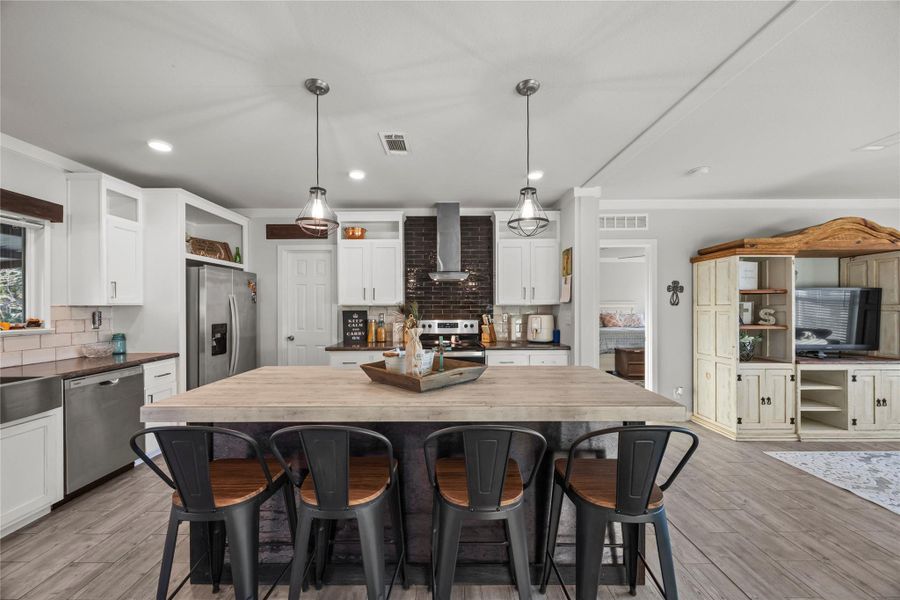 Kitchen featuring backsplash, decorative light fixtures, a kitchen bar, stainless steel appliances, and crown molding