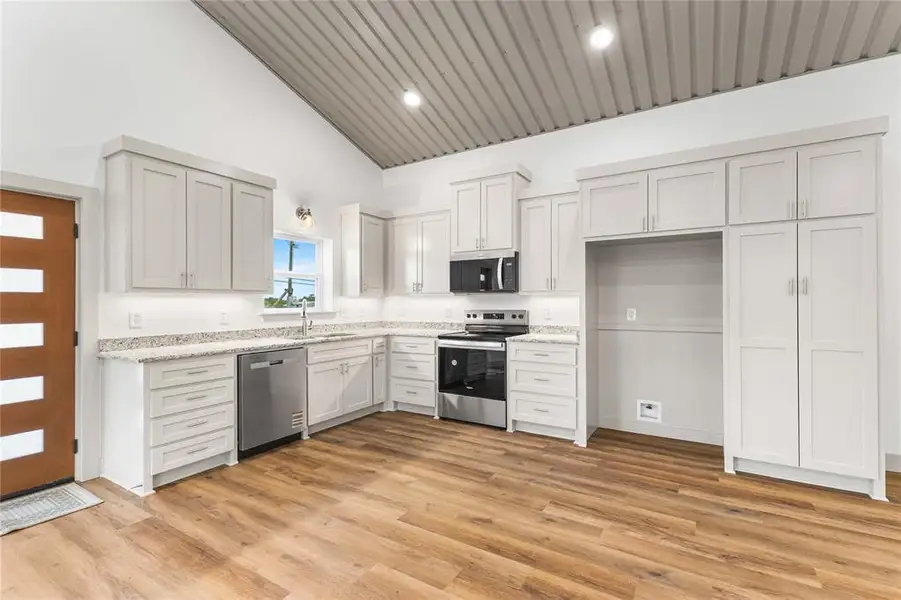 Kitchen with appliances with stainless steel finishes, a sink, high vaulted ceiling, light wood-type flooring, and light stone counters Kitchen with appliances with stainless steel finishes, a sink, high vaulted ceiling, light wood-type flooring, and light stone counters