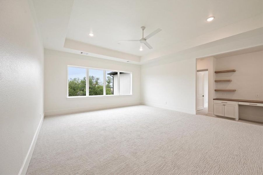 Carpeted empty room with ceiling fan and a tray ceiling