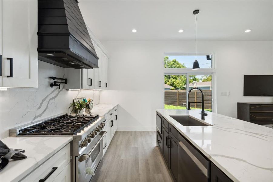 Kitchen featuring sink, decorative light fixtures, white cabinetry, appliances with stainless steel finishes, and custom range hood