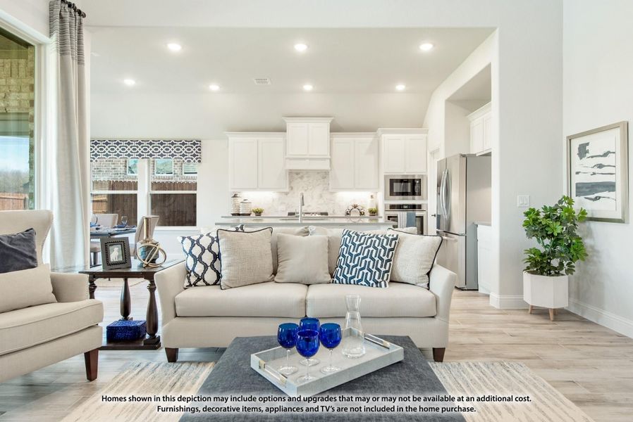 Open-concept living room with beige sofa and light wood floors, open to kitchen with white cabinets and stainless appliances