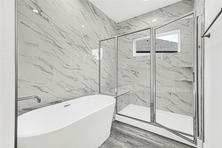 This bathroom features a modern design with a sleek freestanding tub and a spacious glass-enclosed shower. The marble-patterned tiles add elegance, complemented by the dark wood-look flooring. A small window provides natural light. This bathroom features a modern design with a sleek freestanding tub and a spacious glass-enclosed shower. The marble-patterned tiles add elegance, complemented by the dark wood-look flooring. A small window provides natural light.